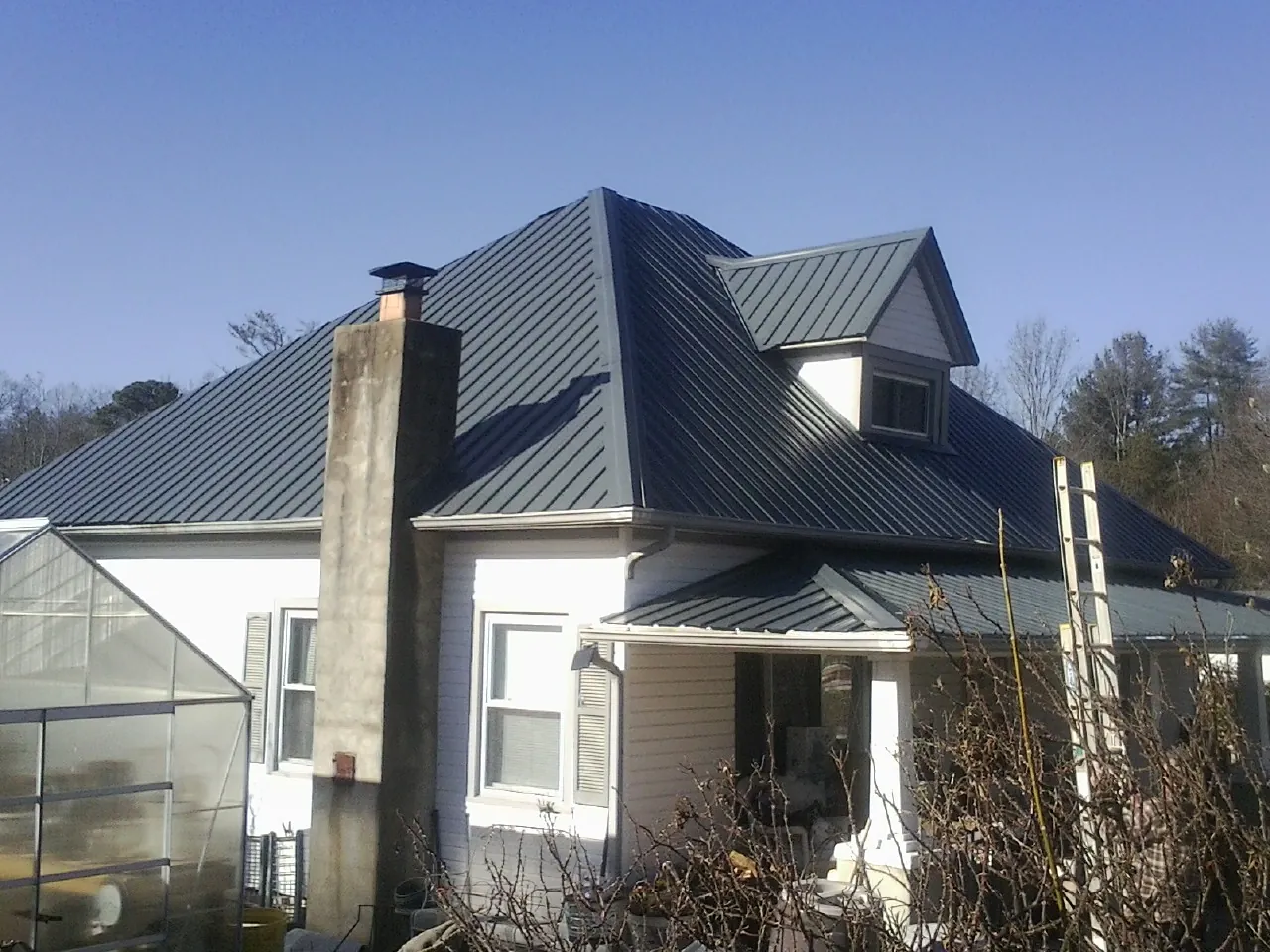 Dark blue standing seam metal roof on a white farmhouse with dormer — Slate & Tile Roof Repair by Roofing Brothers in Hesston