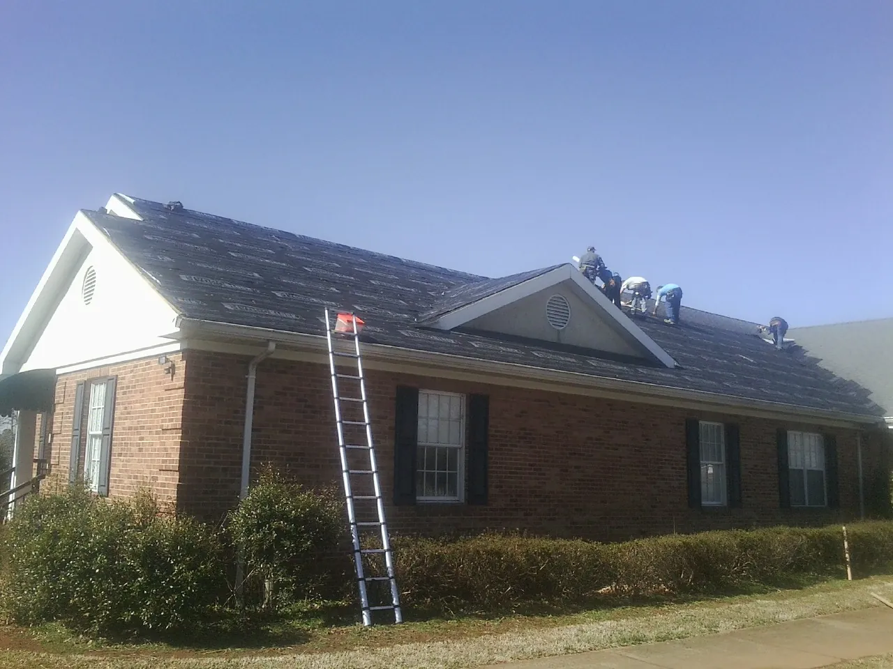 Crew tearing shingles off a brick ranch roof with a ladder set — Emergency Roof Repair work by our crew in Hesston