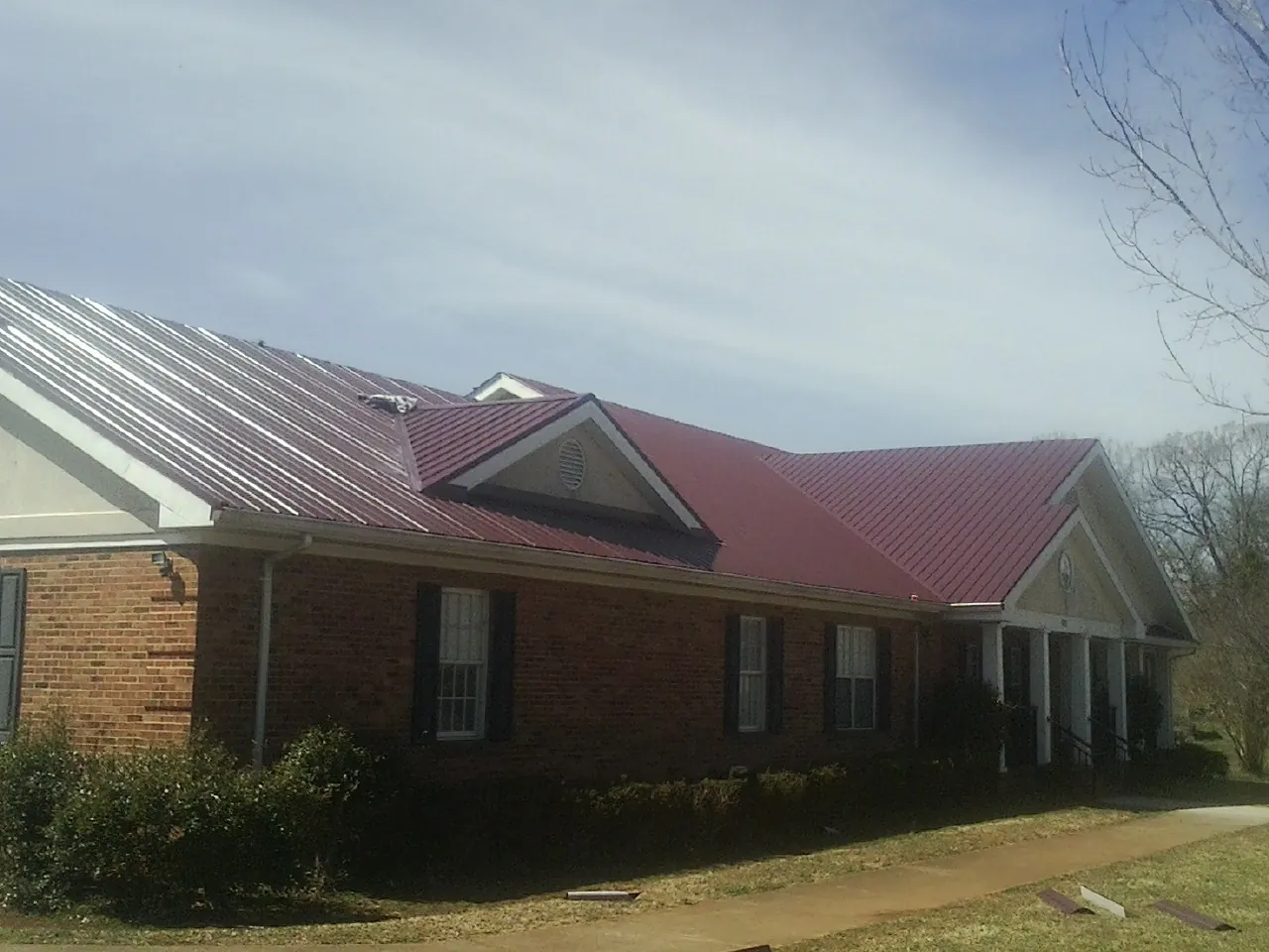 Red metal roof with gabled entries on a long brick building, from a Hail Damage Roof Repair job in Hesston