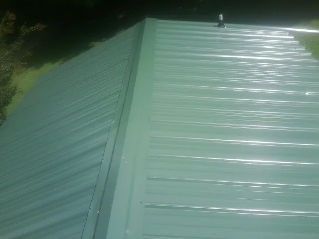 New green metal panels meeting at the ridge of a roof — Flat Roof Repair work by our crew in Hesston