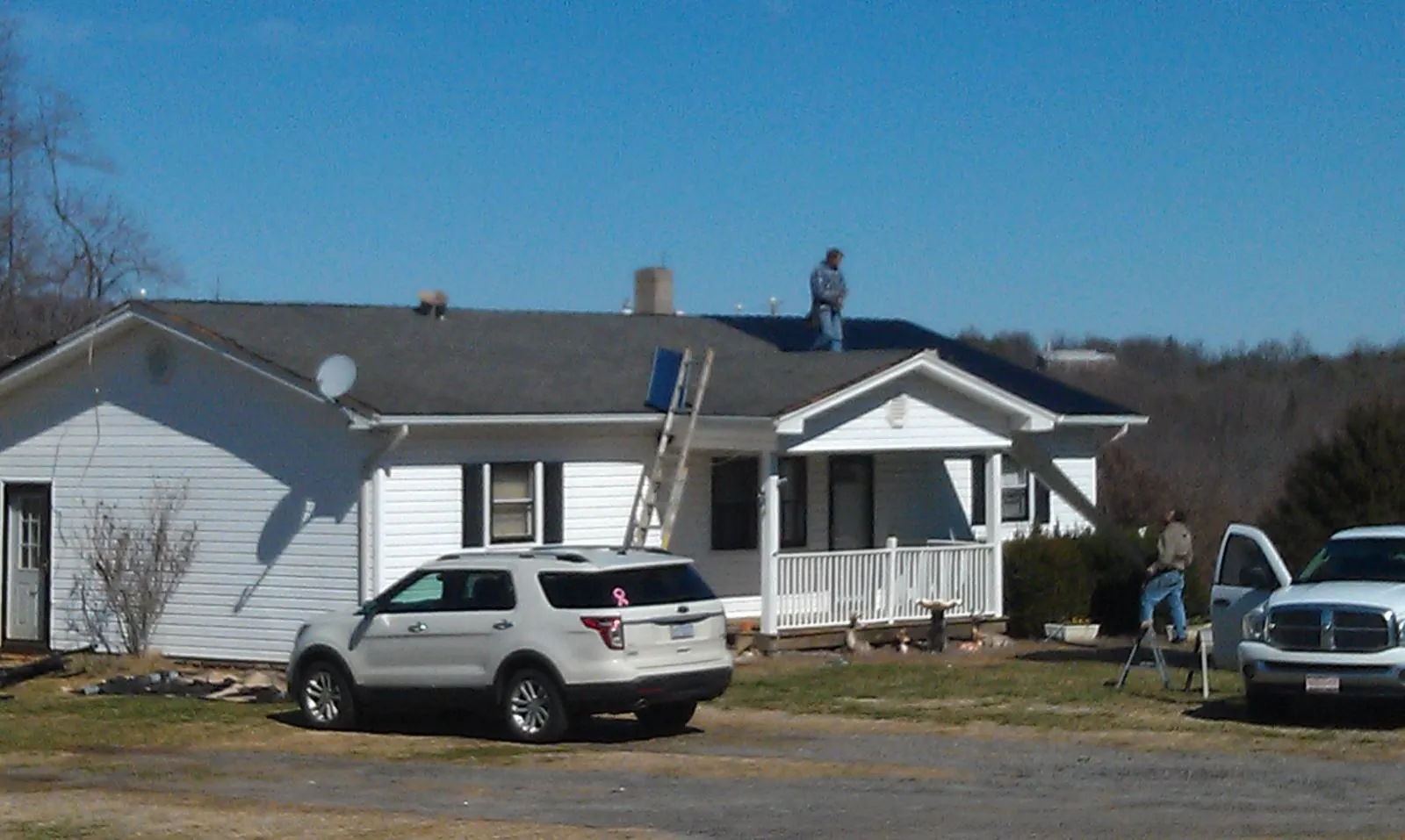 Roofers stripping shingles from a white ranch house roof in Hesston
