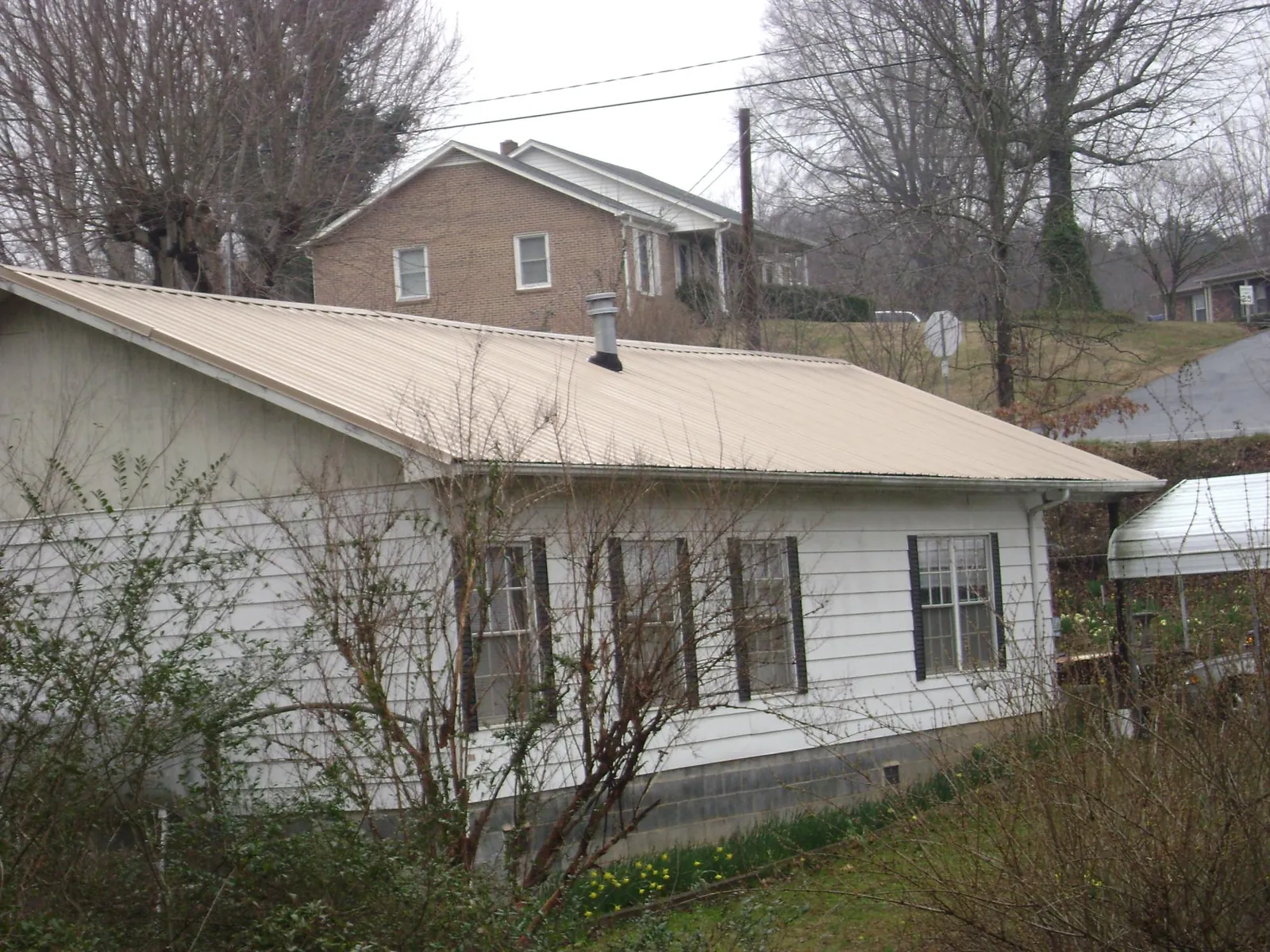 Tan metal roof on a white sided house set into a hillside — Commercial Roofing by Roofing Brothers in Hesston