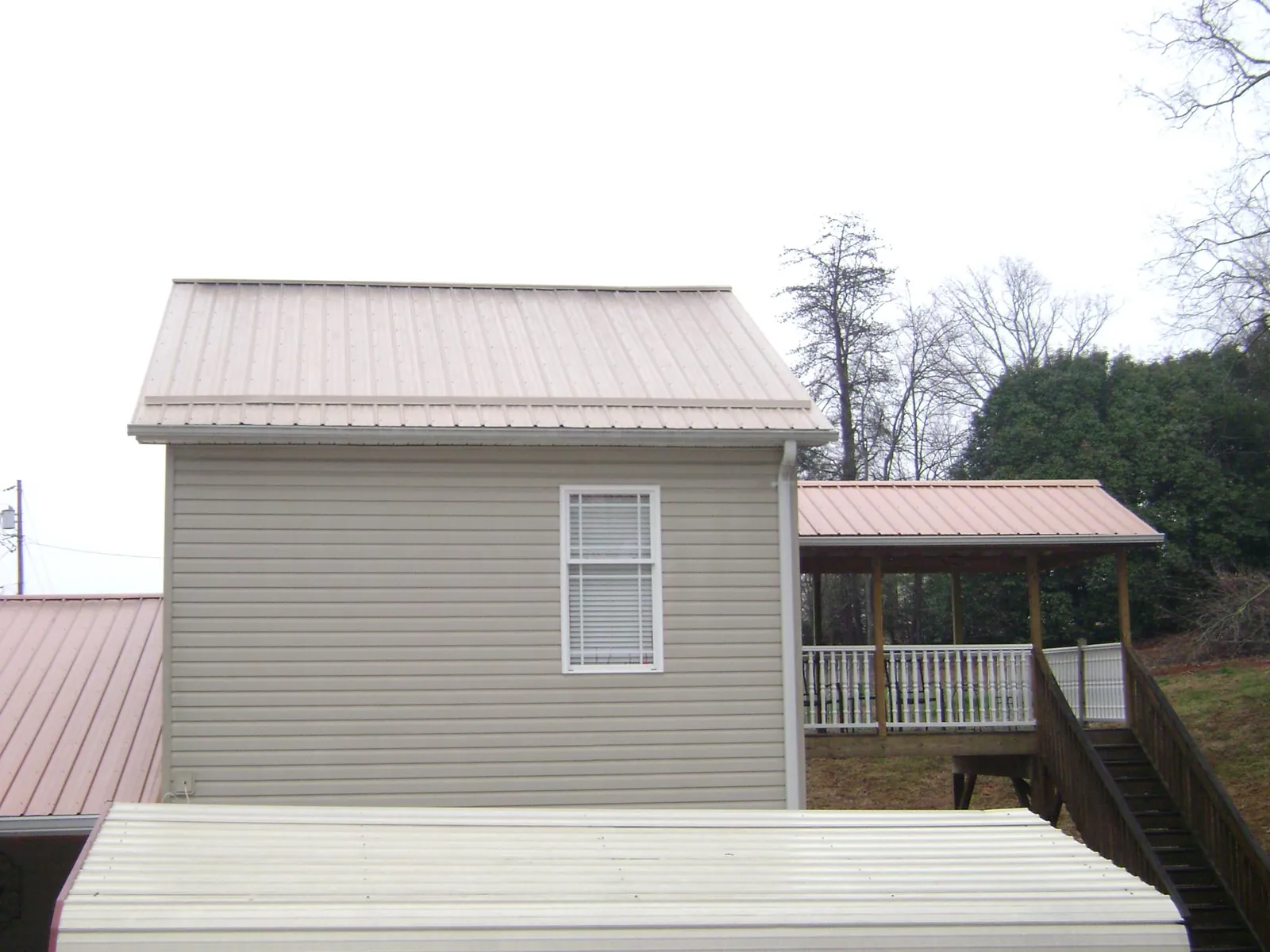 Tan metal roofs on a two story addition and attached porch, from a Roof Replacement job in Hesston